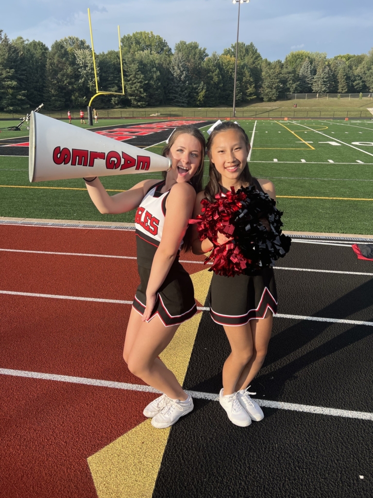 2023 Eden Prairie High School (EPHS) Cheer Captains Maggie Hanson and Jessica Fang dressed in their uniforms standing on a stadium track.